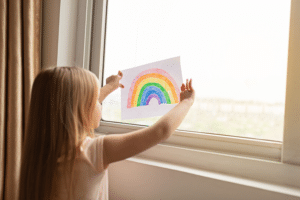 Jeune fille tient un dessin d'arc en ciel dans la fenetre 