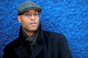 portrait homme devant un mur bleu porte un béret et une écharpe